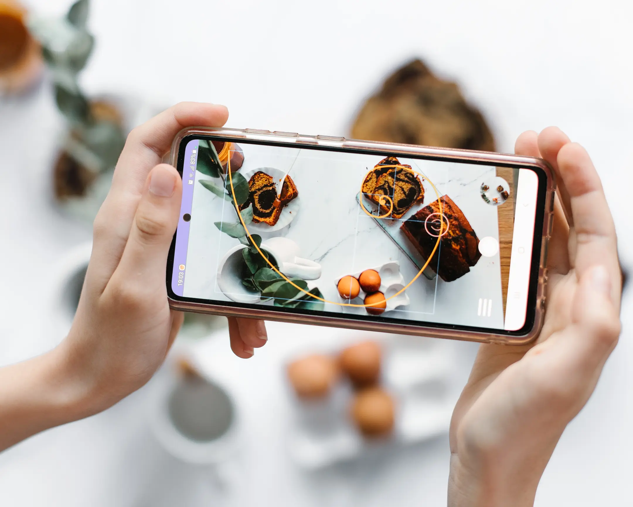 Страхотно фото приложение - златна спирала. Човек, който държи телефон, демонстриращ приложението Awesome Photo и златна спирала, торти, яйца и листа.